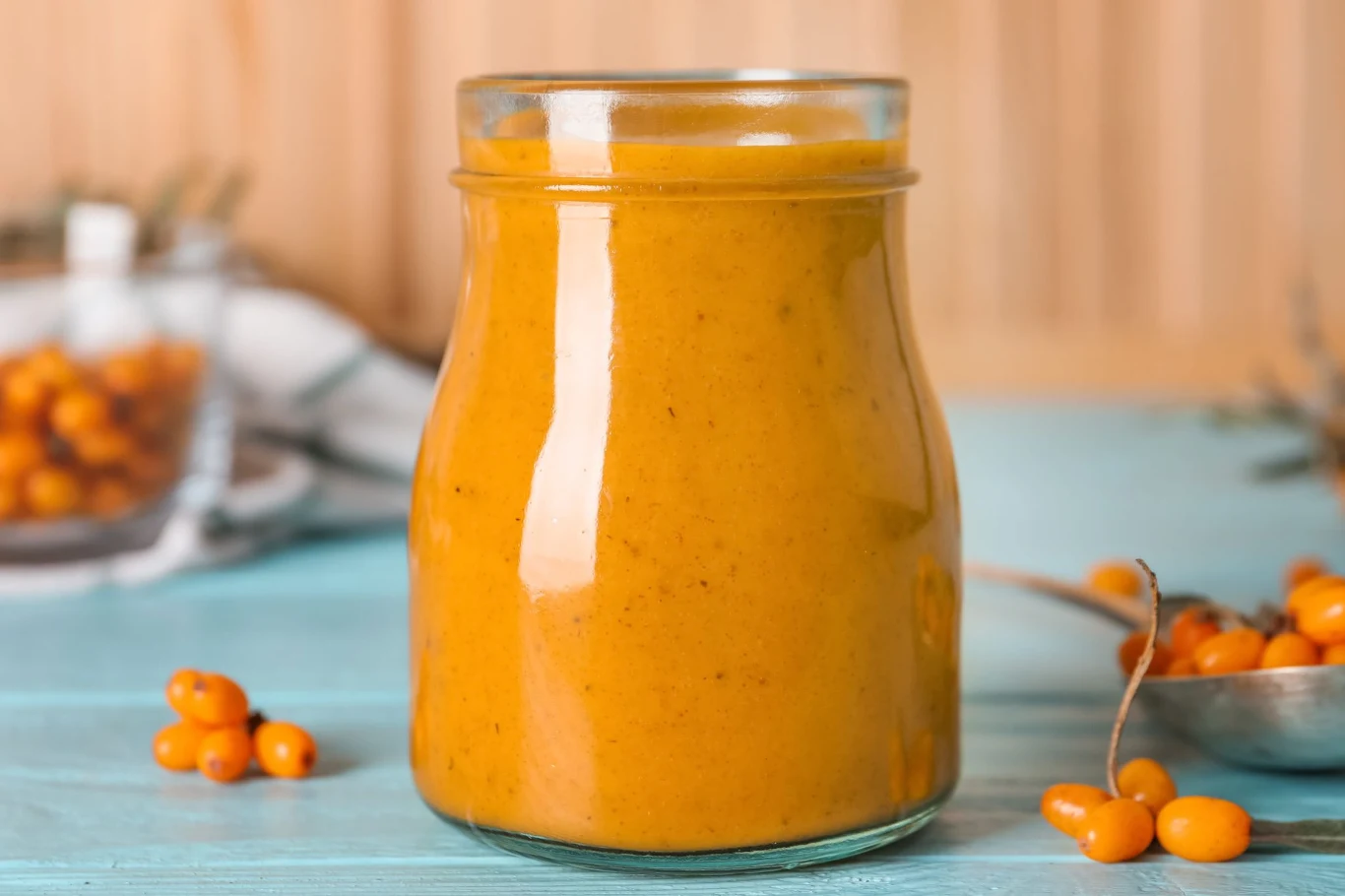 Rokitnik może być świetnym dodatkiem do koktajli Słoik z gęstym kremem z rokitnika, obok łyżka i stolik z rozsypanymi świeżymi owocami rokitnika.