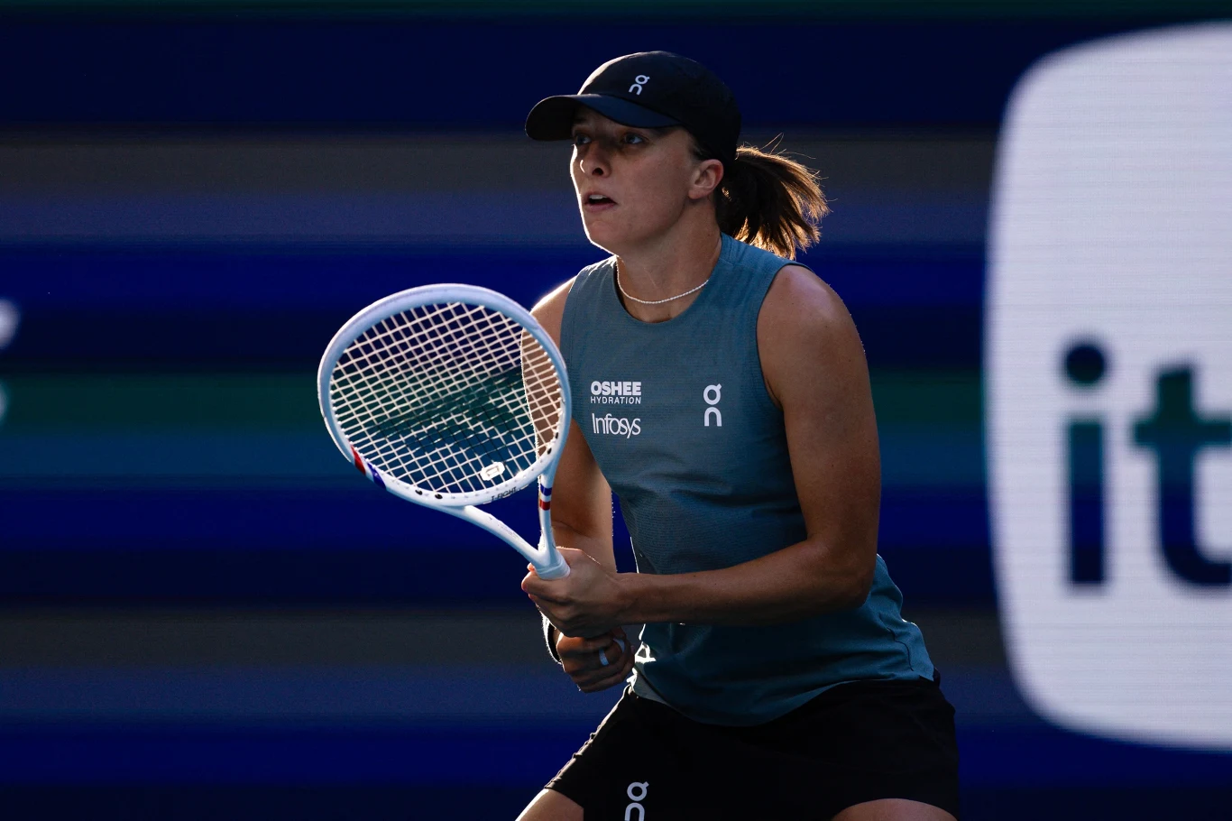 kobieta w sportowym stroju tenisowym skoncentrowana podczas gry, trzymająca rakietę oraz gotowa do odbioru piłki na korcie przy sztucznym oświetleniu