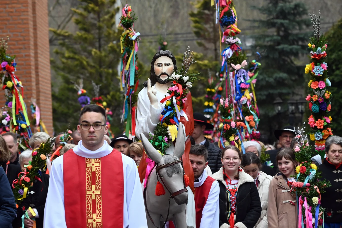 procesja religijna z figurą Jezusa na osiołku otoczoną uczestnikami, wśród których widoczne są barwne palmy wielkanocne udekorowane wstążkami i kwiatami