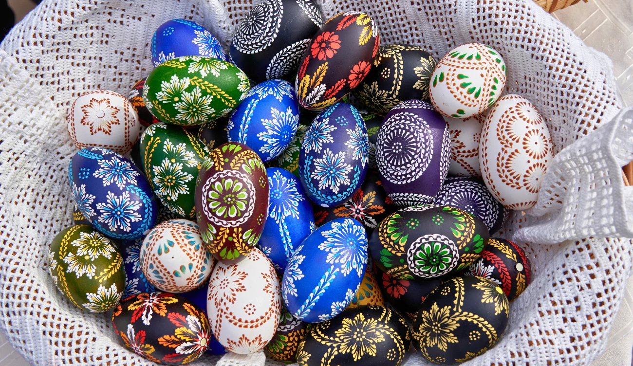 Jak ozdabiano jajka w poszczególnych regionach Polski? Kolorowe pisanki z tradycyjnymi wzorami ułożone w białym, ażurowym koszyku.