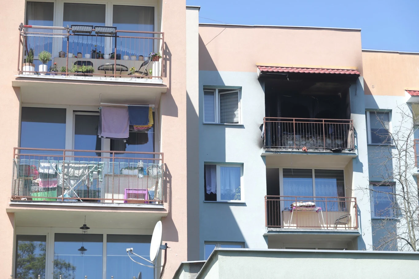 osmalony balkon i czarne ślady po pożarze na drugim piętrze budynku mieszkalnego, w sąsiedztwie zadbanych balkonów z roślinami i praniem