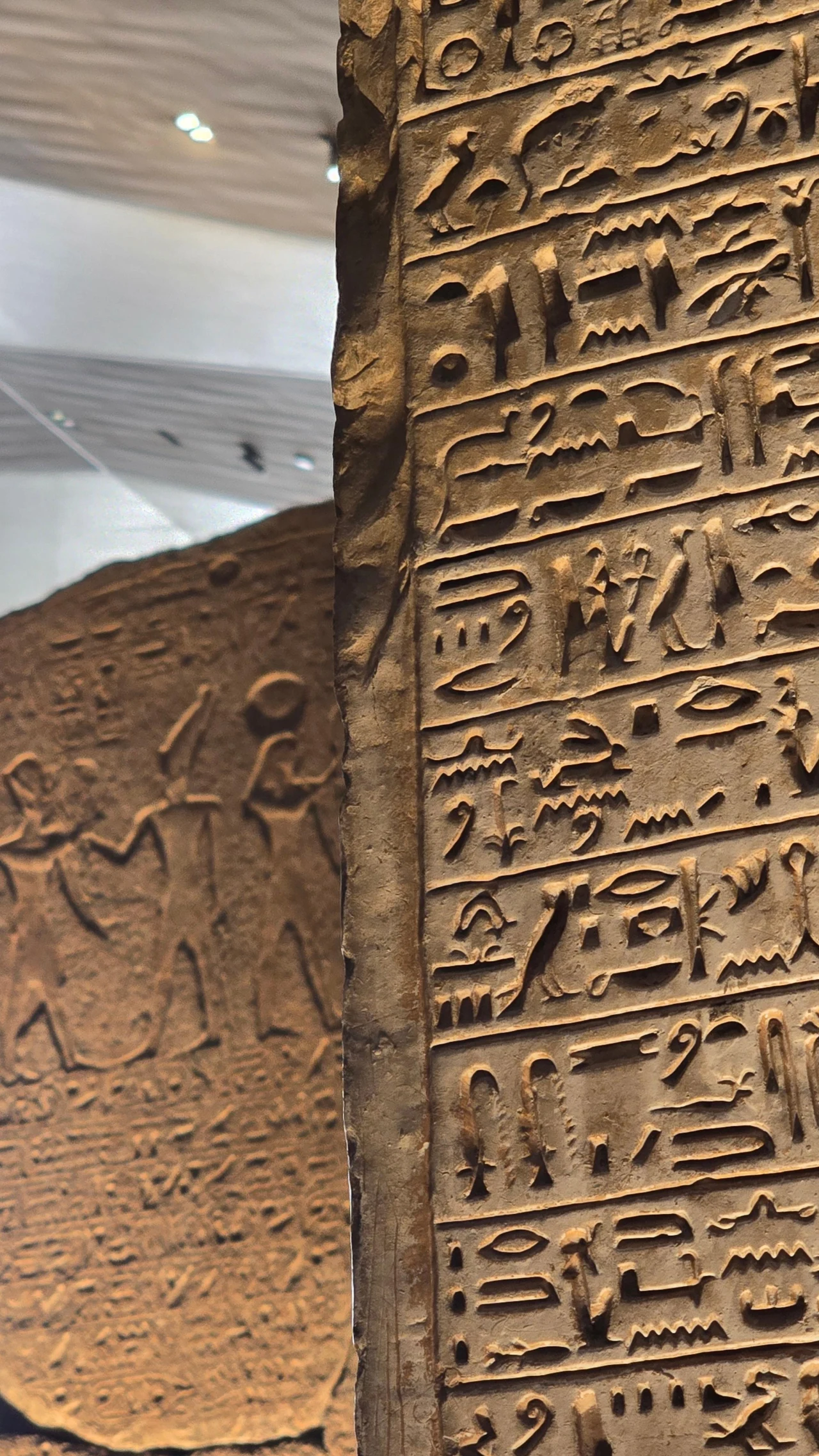 kamienna tablica pokryta starożytnymi egipskimi hieroglifami, w tle płaskorzeźby przedstawiające ludzkie postacie