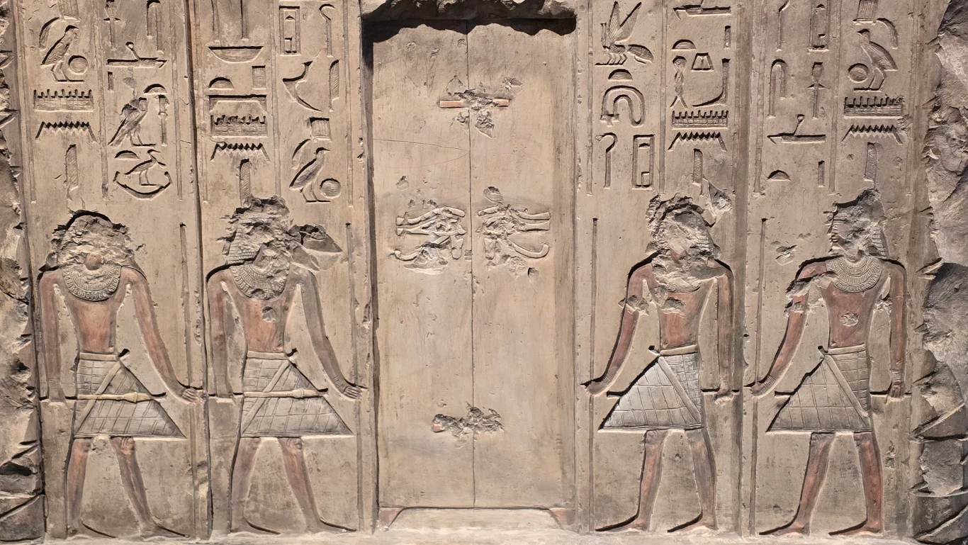 kamienna płaskorzeźba z egipskimi hieroglifami oraz postaciami dwóch ludzi po obu stronach dużych drzwi, każda figura zwrócona jest twarzą w stronę środka, ubrana w tradycyjny strój i nosząca charakterystyczne fryzury