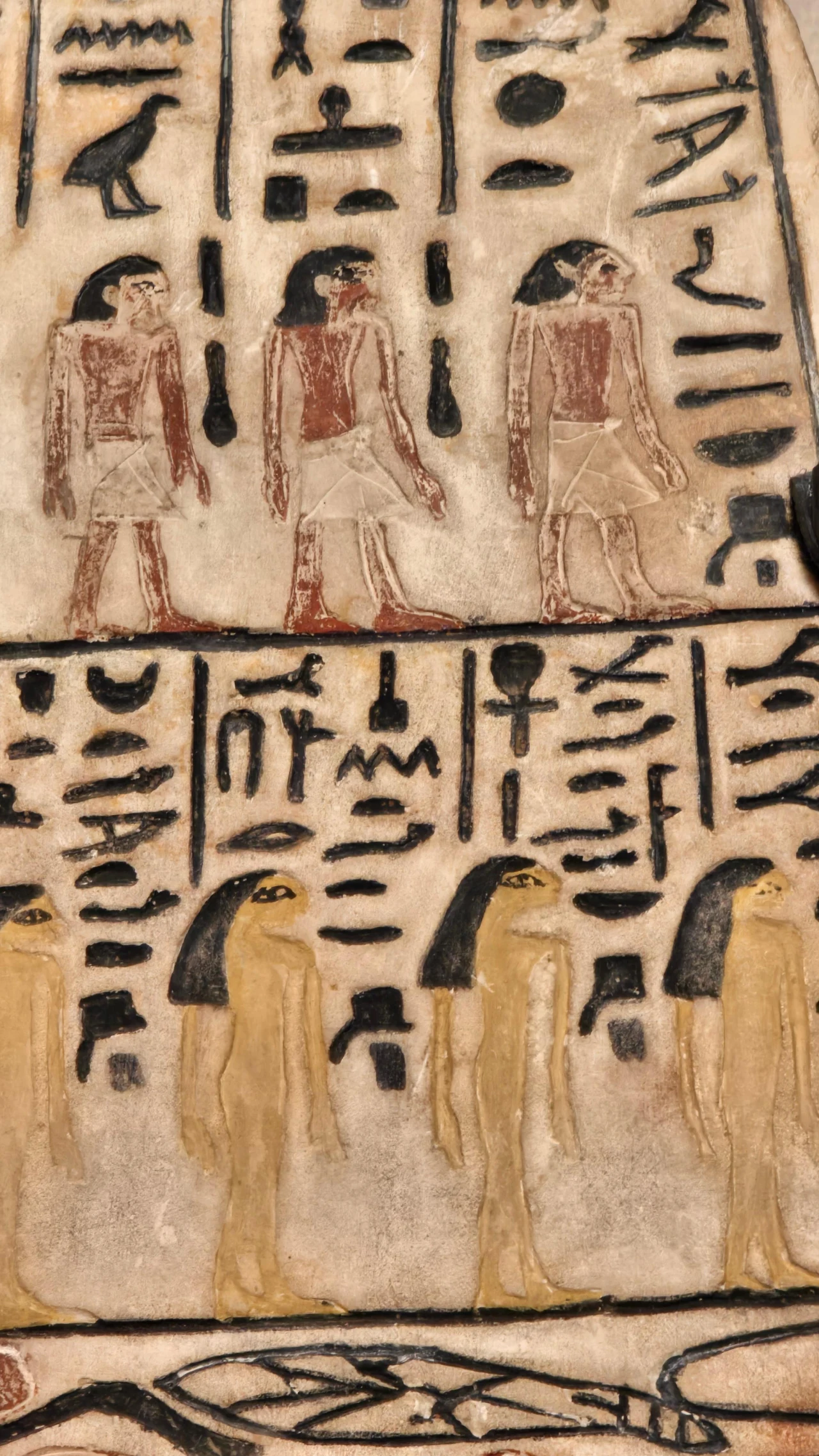 cztery postacie ludzkie w egipskich strojach z ciemnymi włosami, otoczone hieroglifami na tle beżowego kamienia; poniżej znajdują się cztery postacie z ciemnymi perukami w jaśniejszych ubraniach, również wśród hieroglifów