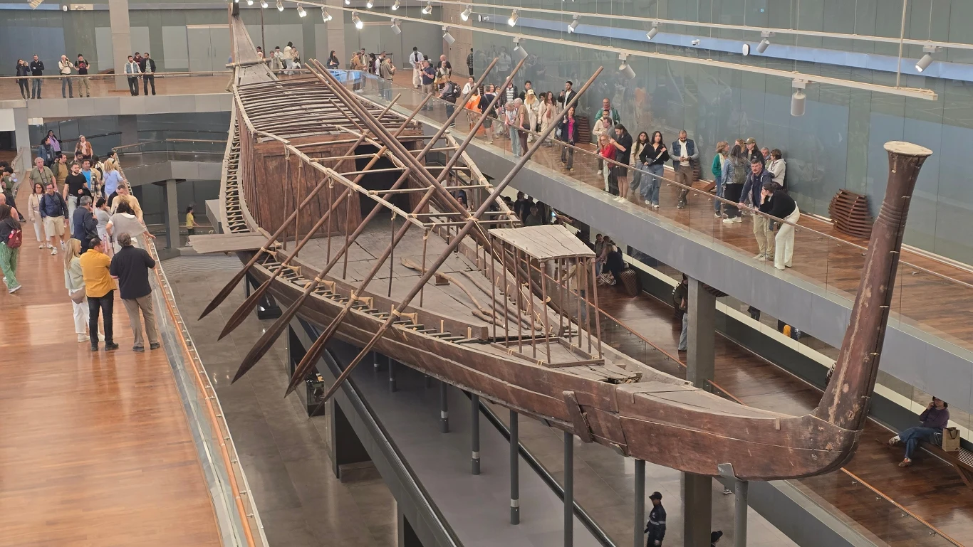 duży, starożytny drewniany statek eksponowany w muzeum, otoczony przez spacerujących zwiedzających na kilku poziomach, konstrukcja łodzi zachowała się w dobrym stanie, jej długi, smukły kształt oraz charakterystycznie wygięty dziób i rufa przyciągają u...