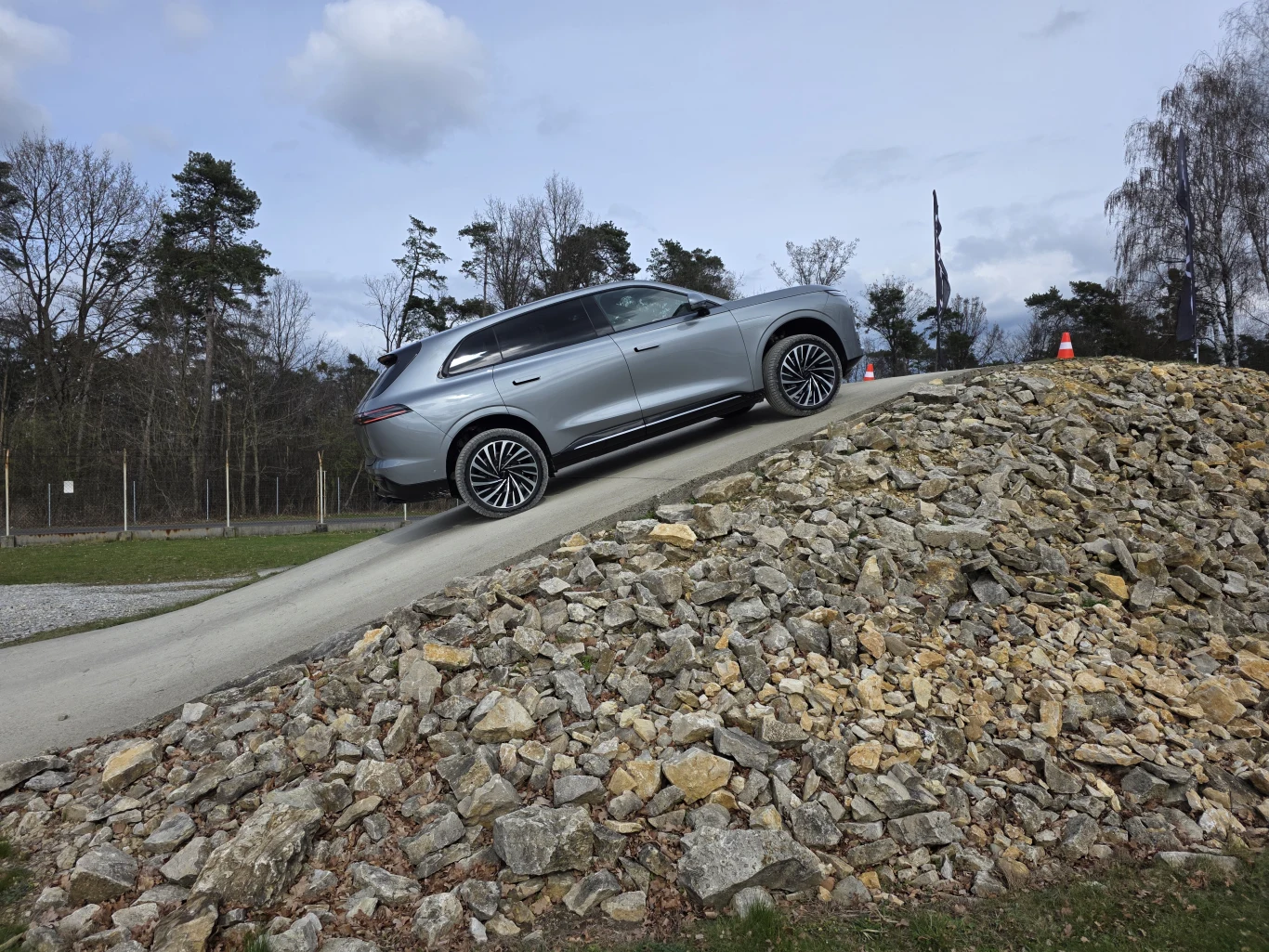 srebrny SUV wjeżdżający pod stromą, utwardzoną rampę otoczoną kamieniami, w tle drzewa i pachołki wyznaczające tor