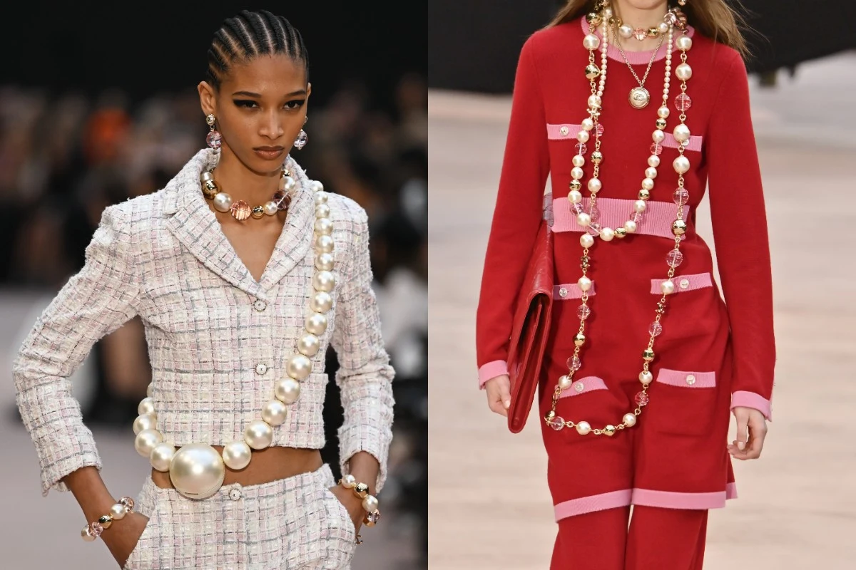 Dwie modelki w stylizacjach haute couture, jedna w białym, tweedowym kostiumie z wyrazistym naszyjnikiem z dużych pereł, druga w czerwonym komplecie ozdobionym długimi sznurami dużych pereł i perłowymi bransoletkami, kontrastujące kolory i wyraziste do...