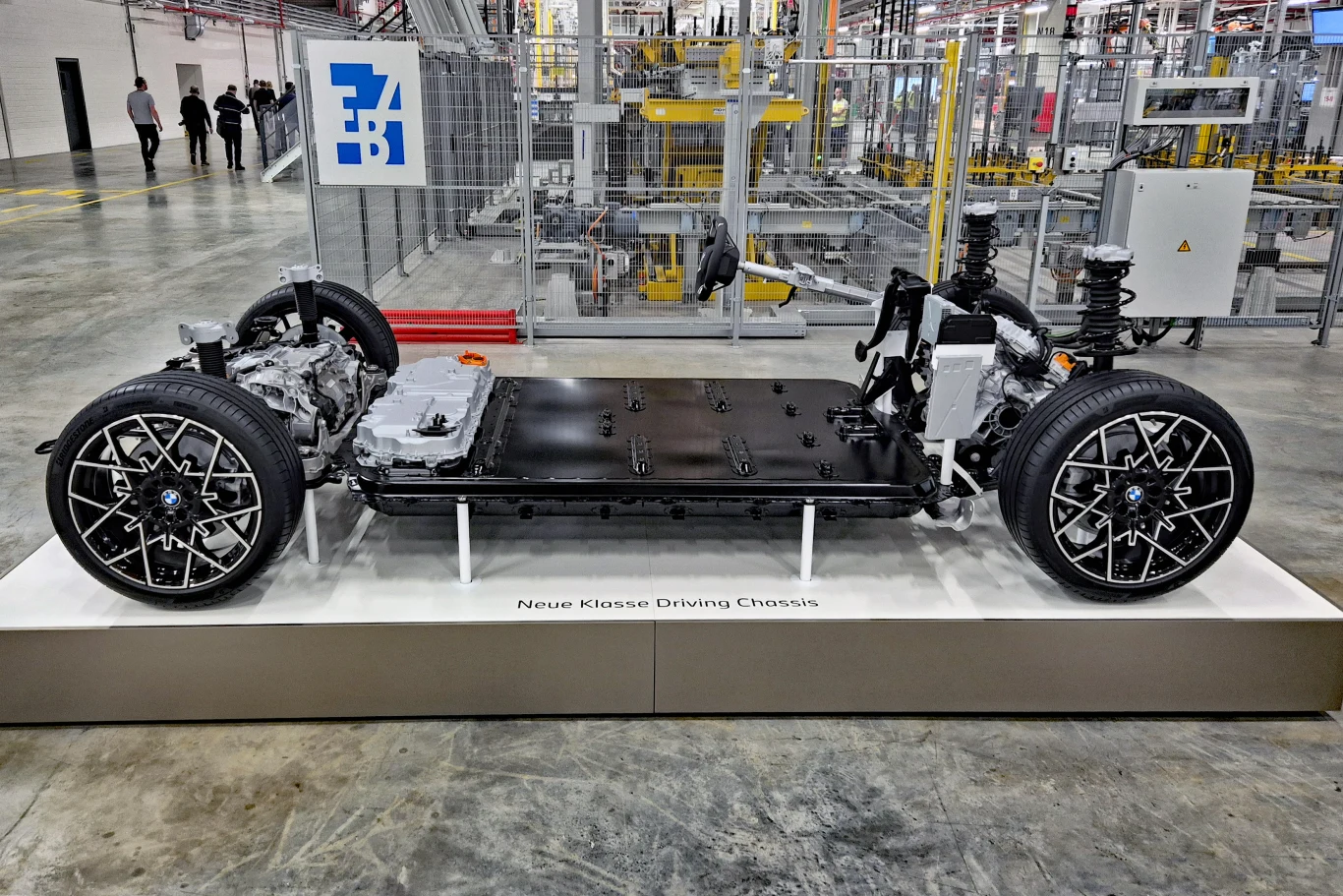 platforma podłogowa samochodu elektrycznego z zamontowanym akumulatorem, silnikami elektrycznymi, zawieszeniem oraz felgami, umieszczona na ekspozycji w hali produkcyjnej