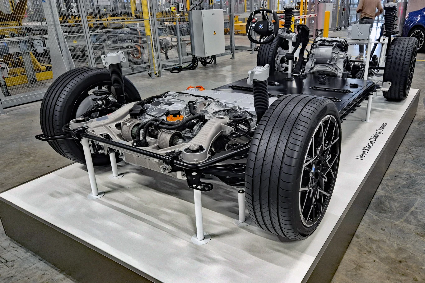 platforma samochodu elektrycznego z widocznym zespołem napędowym, zawieszeniem oraz kołami, prezentowana na podwyższeniu w hali produkcyjnej