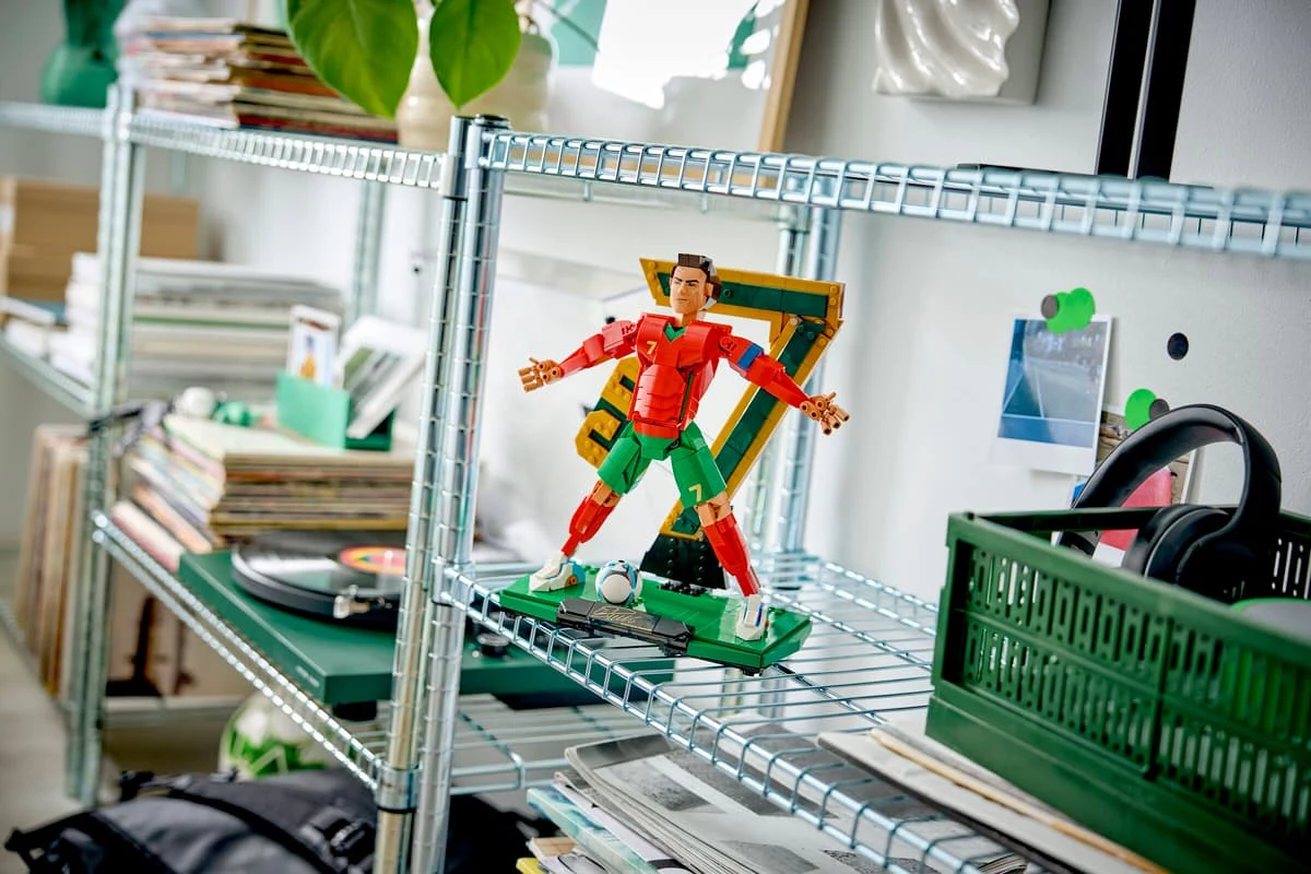 figurka piłkarza z klocków LEGO ustawiona na metalowym regale, w otoczeniu płyt winylowych, gazet, słuchawek i zielonego pudełka