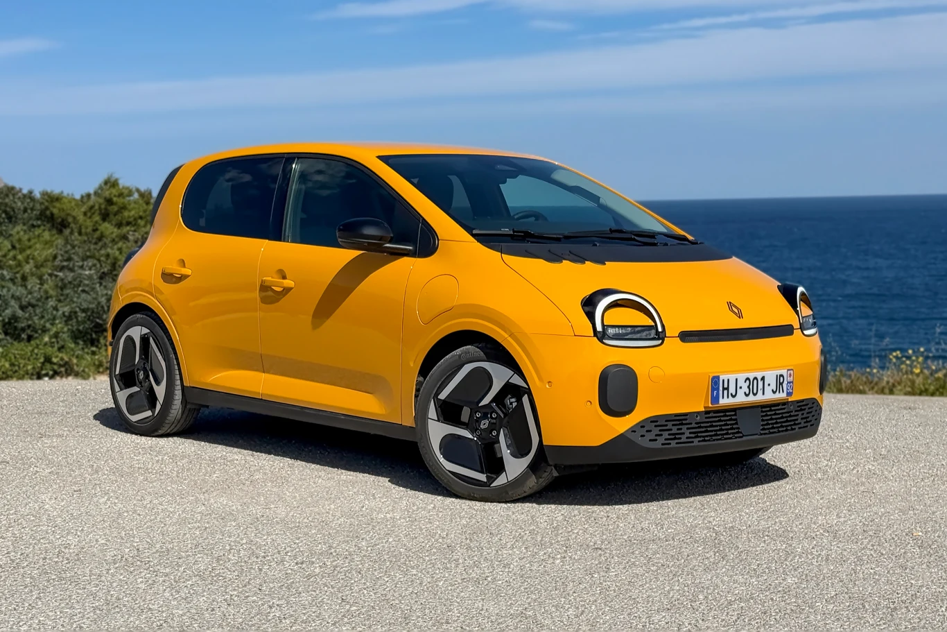 Nowe elektryczne Twingo E-Tech. Zapowiedź wielkiego powrotu segmentu A? żółty samochód osobowy typu hatchback z nowoczesnymi reflektorami i dużymi felgami, zaparkowany na jasnej nawierzchni przy wybrzeżu z widokiem na morze w tle