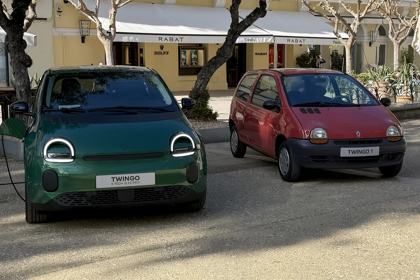 Dwa samochody Renault Twingo stoją obok siebie na zewnątrz: po lewej nowoczesna, zielona wersja elektryczna z podświetlonymi światłami, po prawej starszy, czerwony model z lat 90.