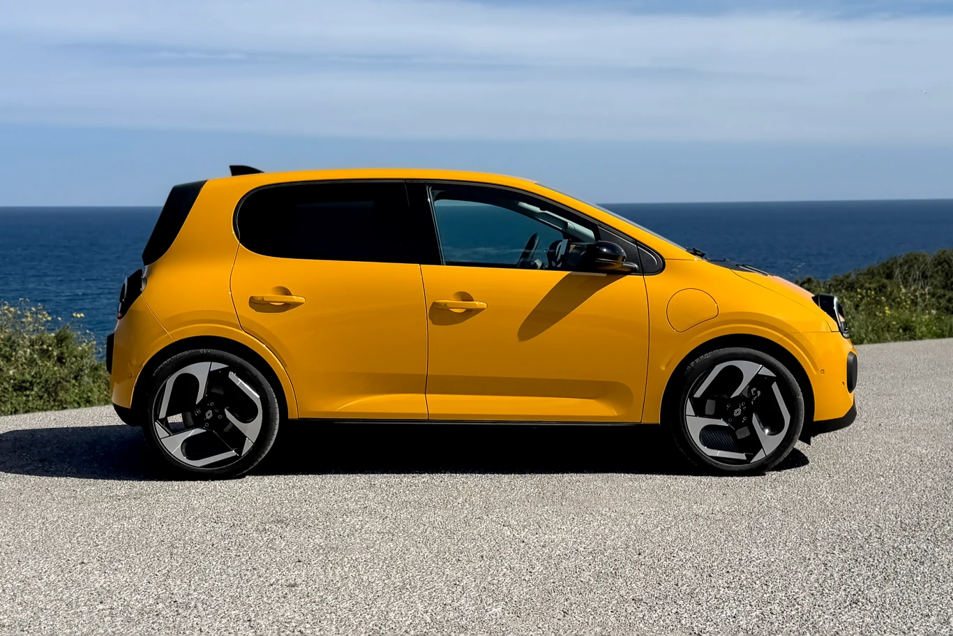 żółty samochód osobowy o nowoczesnym designie stoi na asfaltowej drodze, w tle widoczne morze i niebo z delikatnym zachmurzeniem