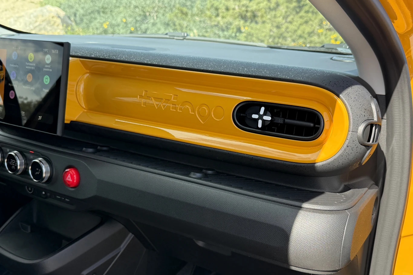 Jaskrawożółta deska rozdzielcza z czarnym nawiewem po prawej stronie, dotykowym ekranem multimedialnym po lewej i logo 'twingo' wytłoczone na środku, poniżej trzy okrągłe pokrętła oraz duży czerwony przycisk na panelu środkowym.