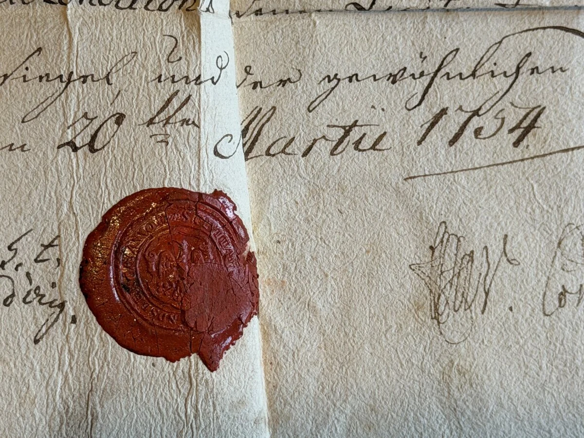 fragment starego dokumentu z widocznym datownikiem z 1854 roku, ręcznym pismem w czarnym atramencie oraz okrągłą pieczęcią lakową w czerwonym kolorze