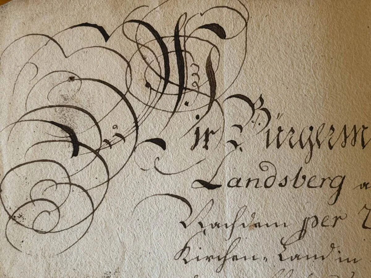 fragment starego dokumentu z ozdobnym, kaligraficznym pismem, na którym dominują duże, skomplikowane zawijasy oraz ciemny tusz na pożółkłym papierze