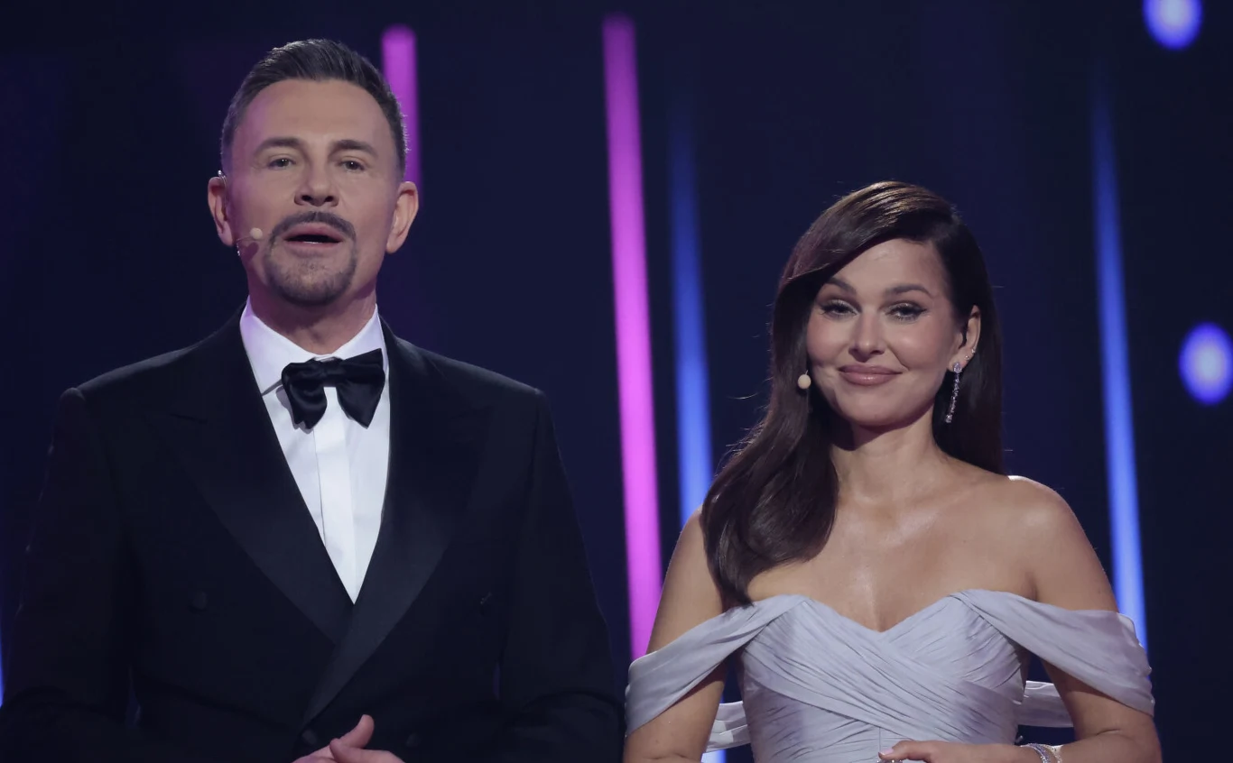 Krzysztof Ibisz, Paulina Sykut-Jeżyna Krzysztof Ibisz i Paulina Sykut-Jeżyna na scenie podczas "Tańca z gwiazdami", elegancko ubrani, oświetleni kolorowymi światłami.