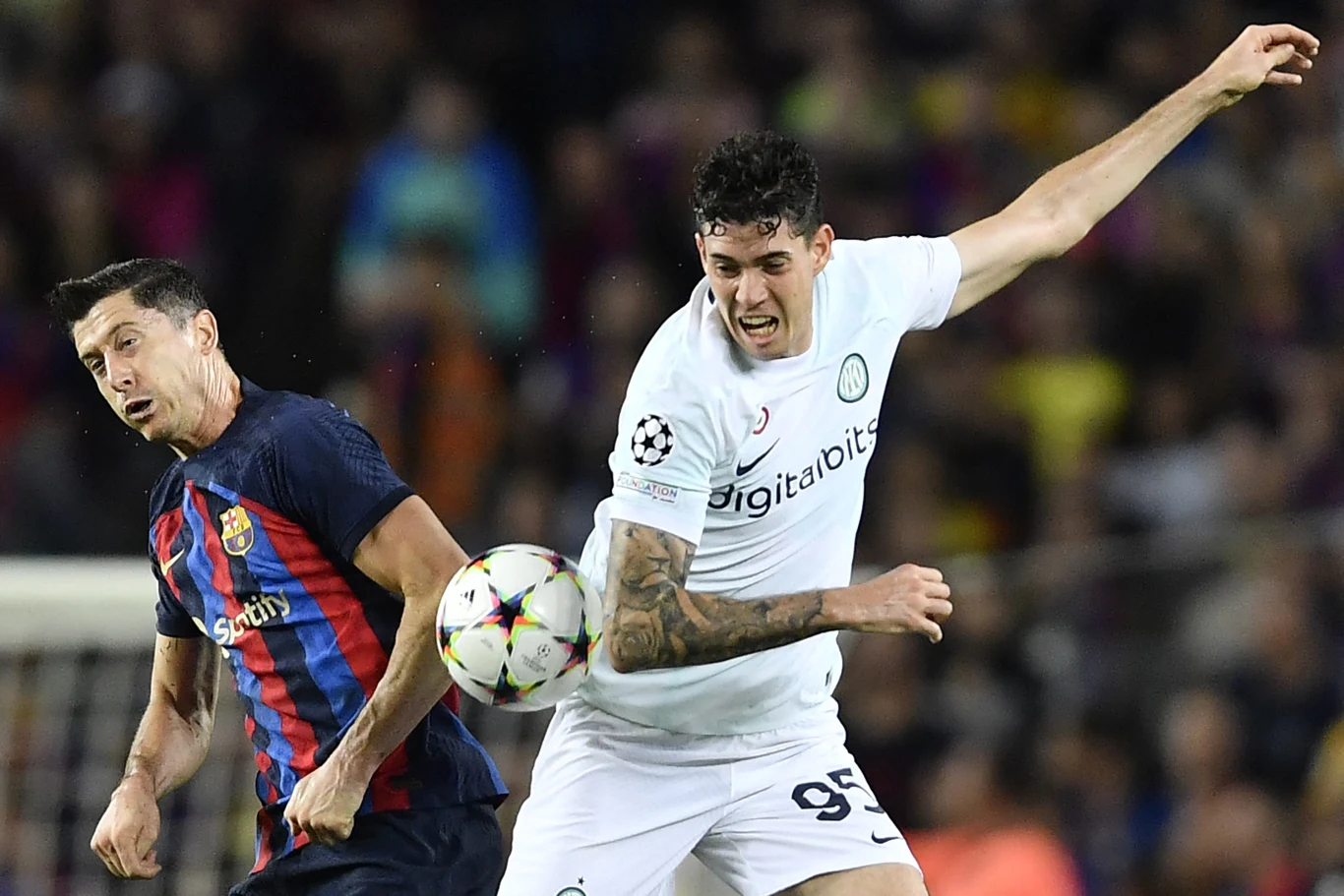 Dwóch piłkarzy rywalizuje o piłkę w trakcie meczu, jeden w stroju FC Barcelony, drugi w stroju Interu Mediolan, intensywna walka w ruchu; tłum kibiców w tle