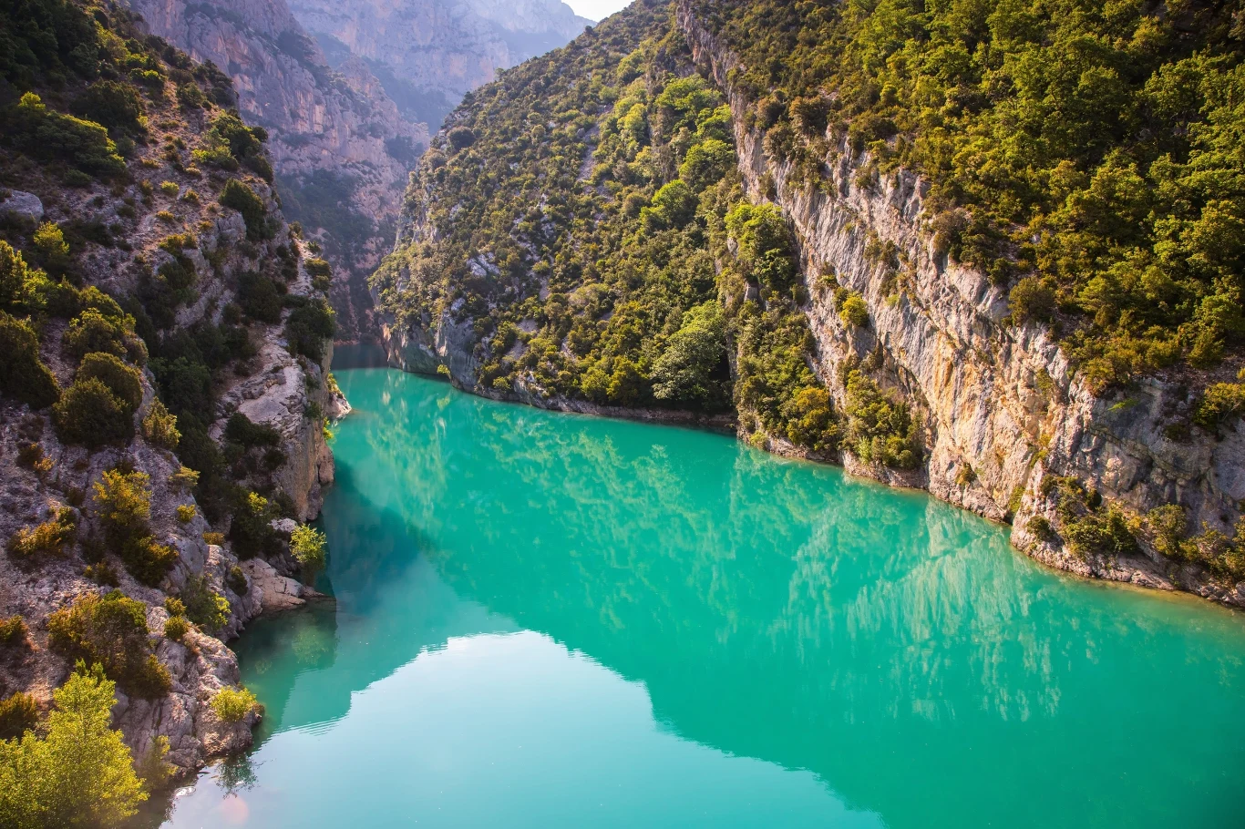 Turkusowa rzeka płynąca w głębokim, skalistym wąwozie, otoczona gęstą zielenią drzew i krzewów pokrywających strome zbocza.