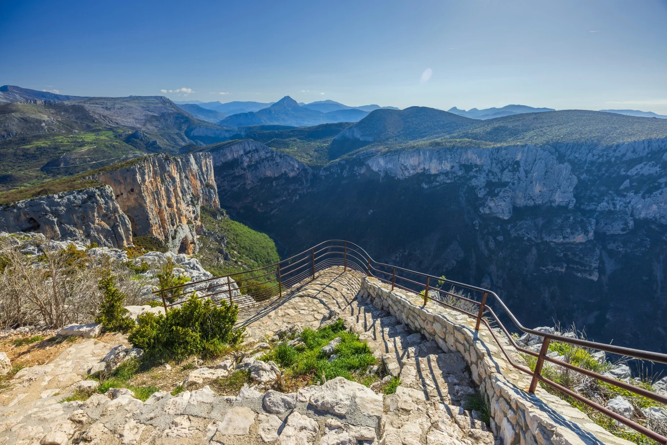 kamienne schody prowadzące w dół w stronę głębokiego kanionu otoczonego majestatycznymi, zalesionymi górami, po lewej pionowe skalne ściany podkreślające malowniczość krajobrazu