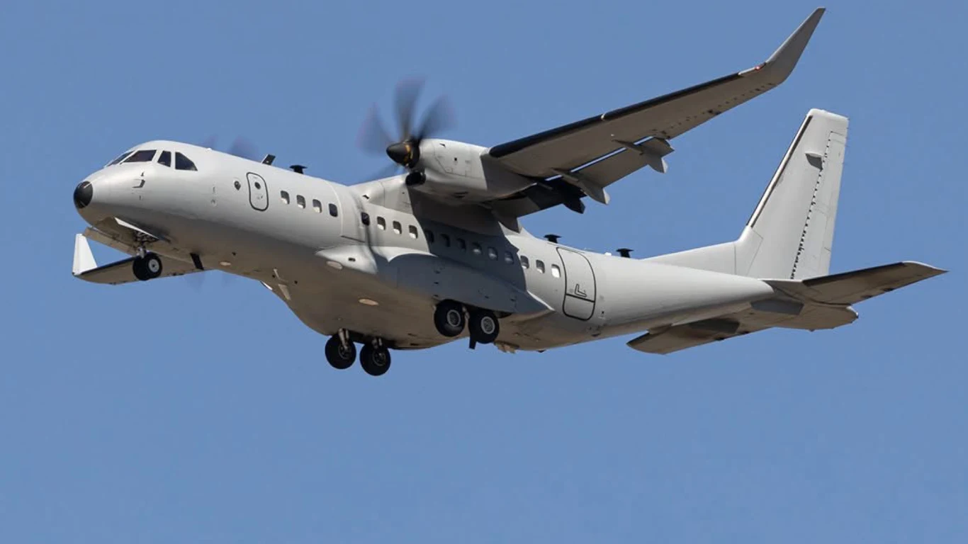 Transportowy samolot turbośmigłowy w locie z wysuniętym podwoziem; w tle błękitne niebo