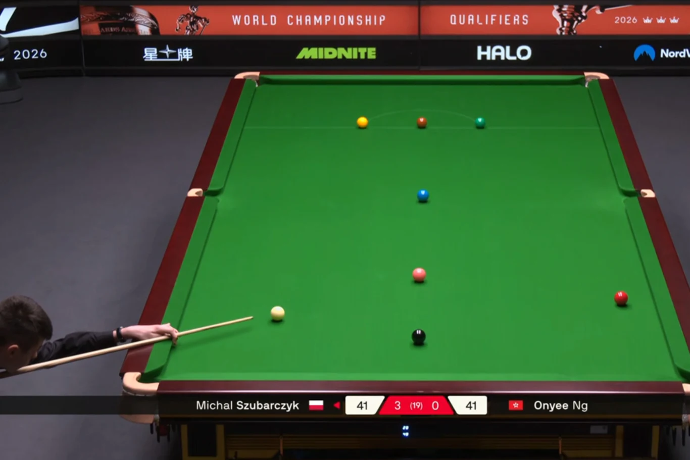 gracz snookera wykonuje uderzenie na profesjonalnym stole, na którym rozmieszczone są kolorowe bile, a wynik meczu pokazywany na ekranie sygnalizuje remis 41:41 między Michałem Szubarczykiem a Onyee Ng podczas kwalifikacji do mistrzostw świata