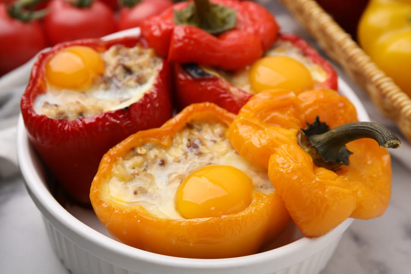 Faszerowane papryki z jajkiem sadzonym połówki żółtej i czerwonej papryki faszerowane mięsem oraz jajkiem, ułożone w białym naczyniu do zapiekania