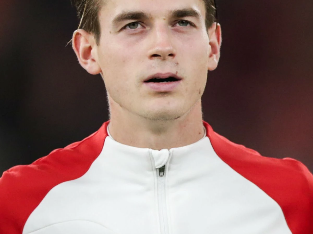 Jakub Kamiński Jakub Kamiński w czerwono-białej sportowej kurtce, patrzy przed siebie z poważnym wyrazem twarzy.