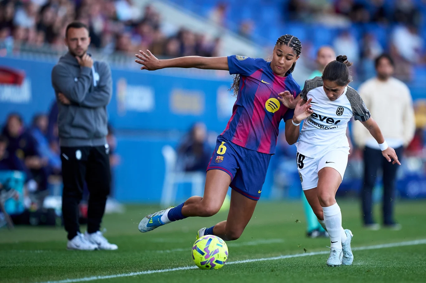 dwie piłkarki rywalizują o piłkę na tle boiska podczas meczu, jedna w bordowo-granatowej koszulce FC Barcelony, druga w biało-czarnym stroju przeciwników; skupienie i intensywność widoczne w ich ruchach i mimice