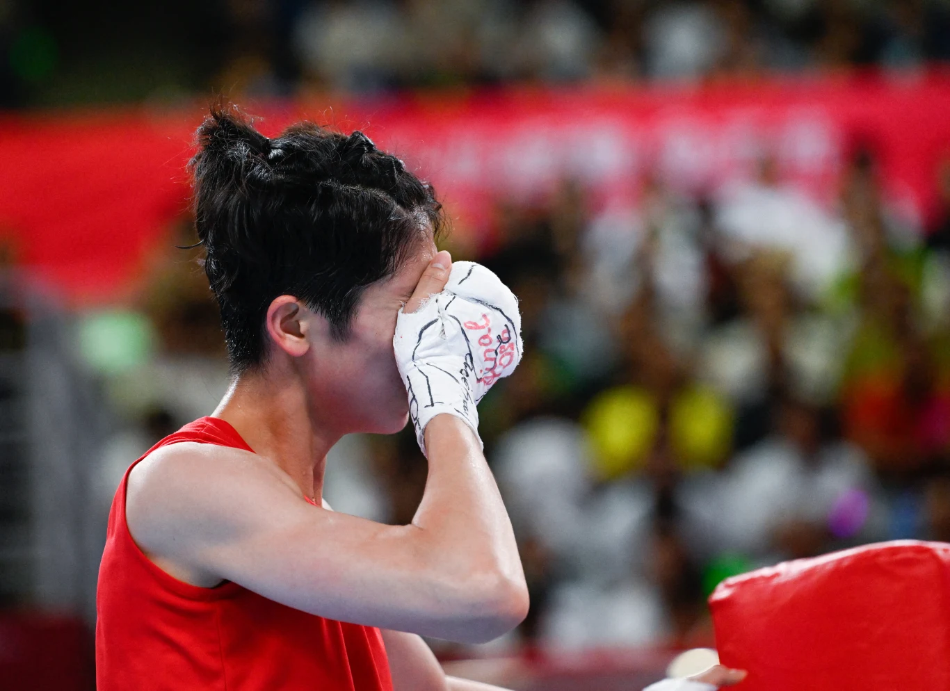 bokserka w czerwonym stroju sportowym trzyma dłoń w rękawicy bokserskiej przy twarzy, sprawiając wrażenie silnych emocji podczas zawodów