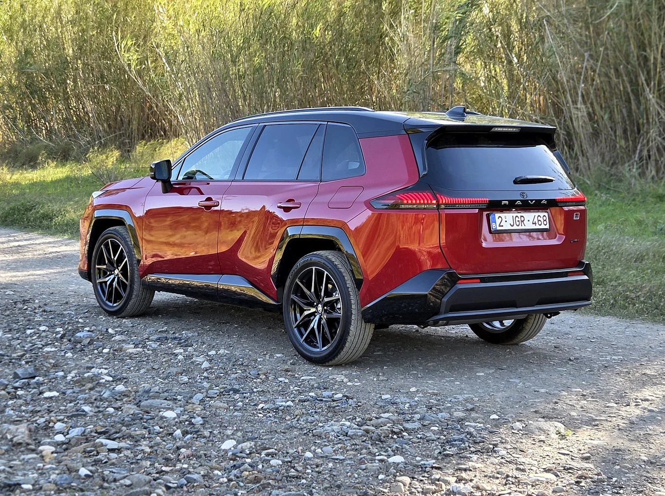 czerwony SUV o nowoczesnej, dynamicznej sylwetce z czarnym dachem i dużymi, sportowymi felgami stoi na kamienistej drodze, otoczony wysoką roślinnością