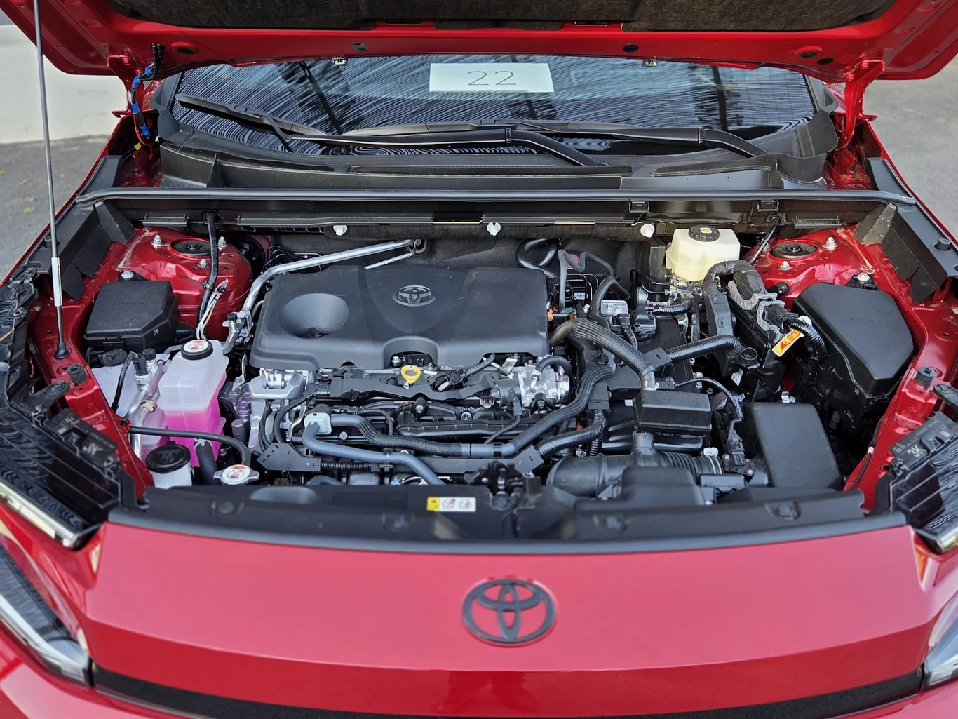 komora silnika czerwonego samochodu Toyota z wyraźnie widocznym silnikiem, zbiornikiem płynu chłodniczego po lewej stronie, akumulatorem po prawej i wieloma elementami osprzętu silnika