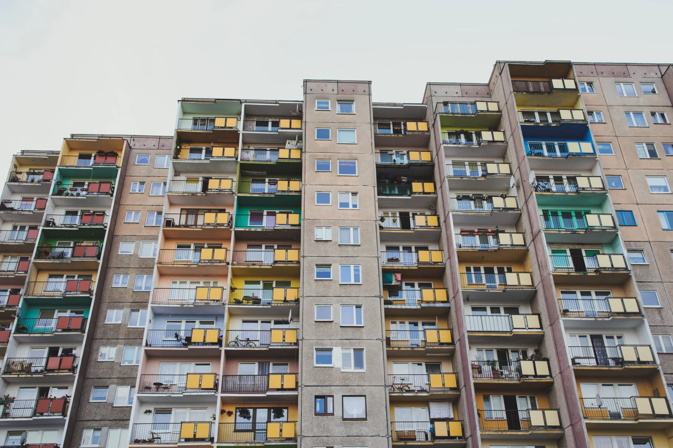 Kto będzie mógł skorzystać z tzw. najmu senioralnego? Wysoki blok mieszkalny z licznymi balkonami o różnorodnych kolorach balustrad i paneli, z widocznymi śladami użytkowania na elewacji budynku.
