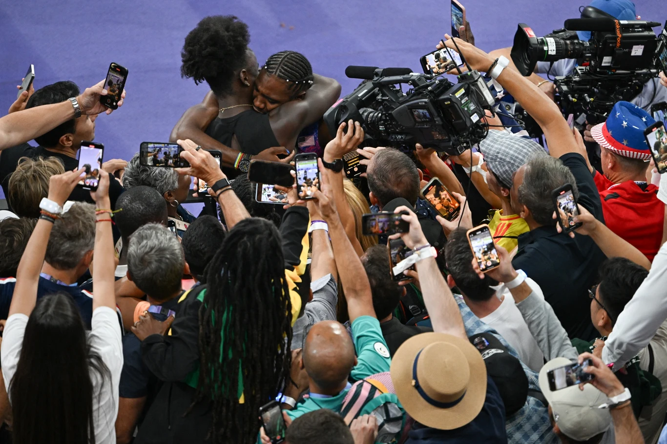 dwie osoby obejmujące się w emocjonalnym uścisku w centrum uwagi licznych fotoreporterów i kibiców, otoczone tłumem ludzi robiących im zdjęcia i nagrywających filmy smartfonami