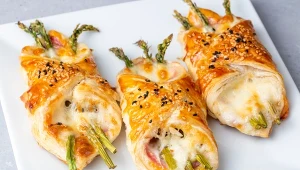 Baked green asparagus with ham and cheese in puff pastry sprinkled with sesame seeds and green basil leaves.