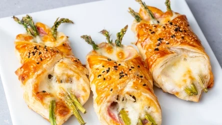 Baked green asparagus with ham and cheese in puff pastry sprinkled with sesame seeds and green basil leaves.