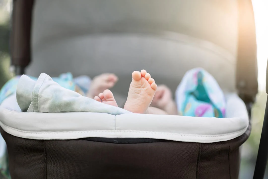 gołe stopy niemowlęcia wystające z wnętrza wózka, otoczone delikatnymi kocykami i miękkim materiałem