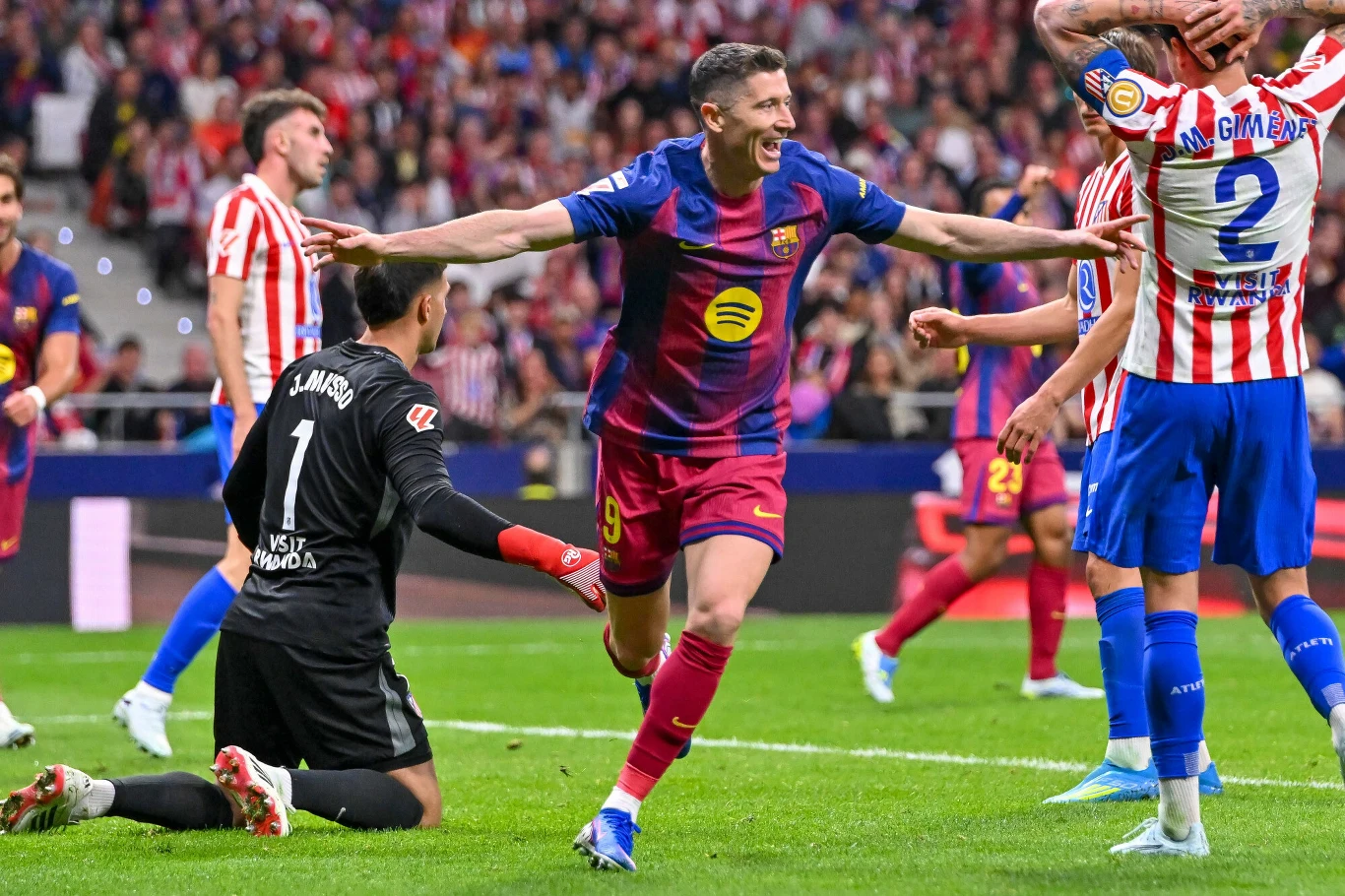 Robert Lewandowski w koszulce Barcelony z uniesionymi ramionami po golu przeciwko Atletico Madryt, bramkarz klęczy na murawie, obrońcy w biało-czerwonych strojach.