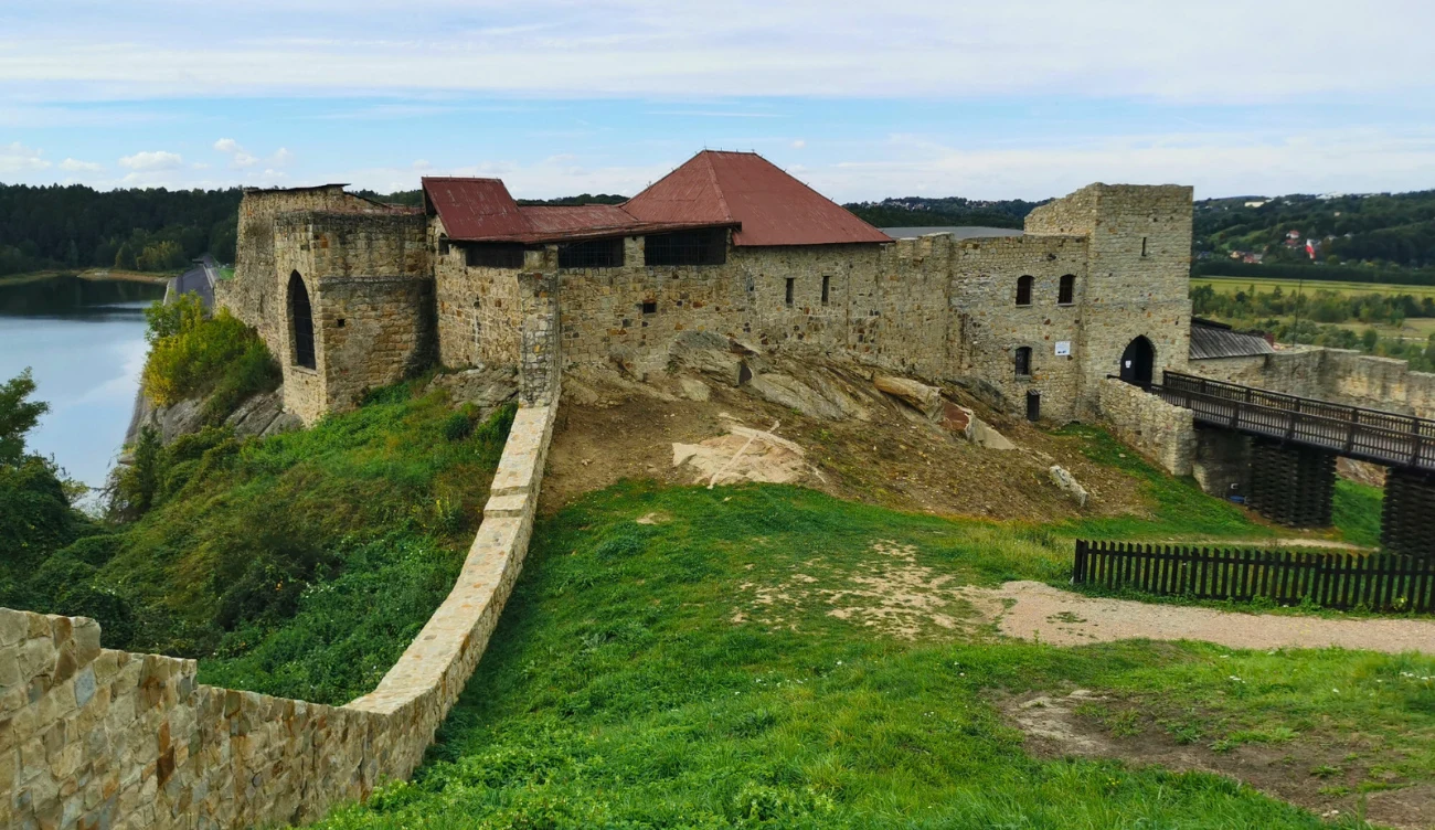 Zamek w Dobczycach - królewska rezydencja nad jeziorem Zamek w Dobczycach na wzgórzu nad jeziorem, ruiny z czerwonym dachem, drewniany most do wejścia