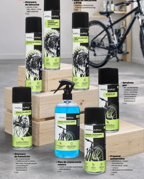 Zestaw specjalistycznych środków czystości i konserwacji KOLARO do roweru ustawionych na drewnianych podestach, obejmujący zmywacz do łańcucha, smar do łańcucha, spray nabłyszczający, płyn do czyszczenia roweru, zmywacz do hamulców oraz preparat uniwer...