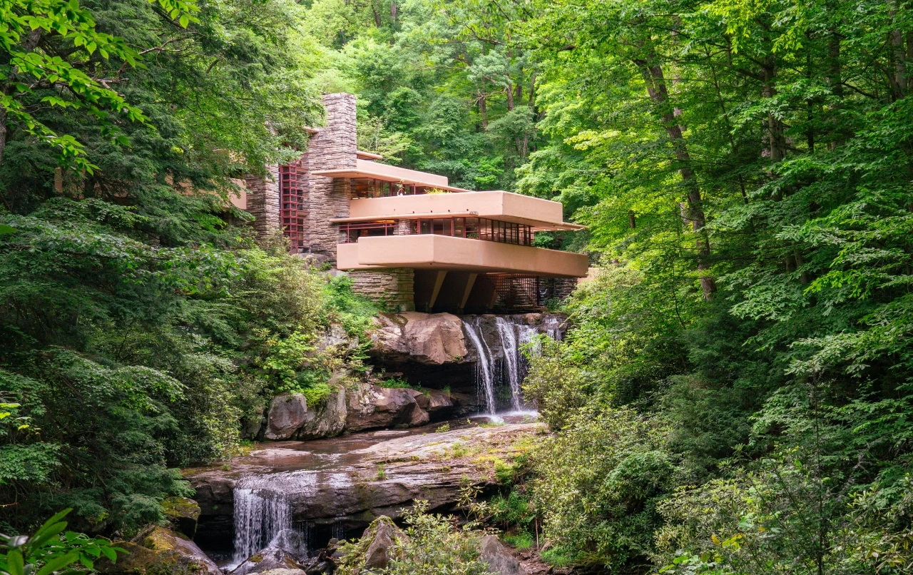Dom fallingwater zaprojektowany przez Franka Lloyda Wrighta Dom Fallingwater Franka Lloyda Wrighta nad wodospadem, otoczony lasem, z kamiennymi ścianami i tarasami.