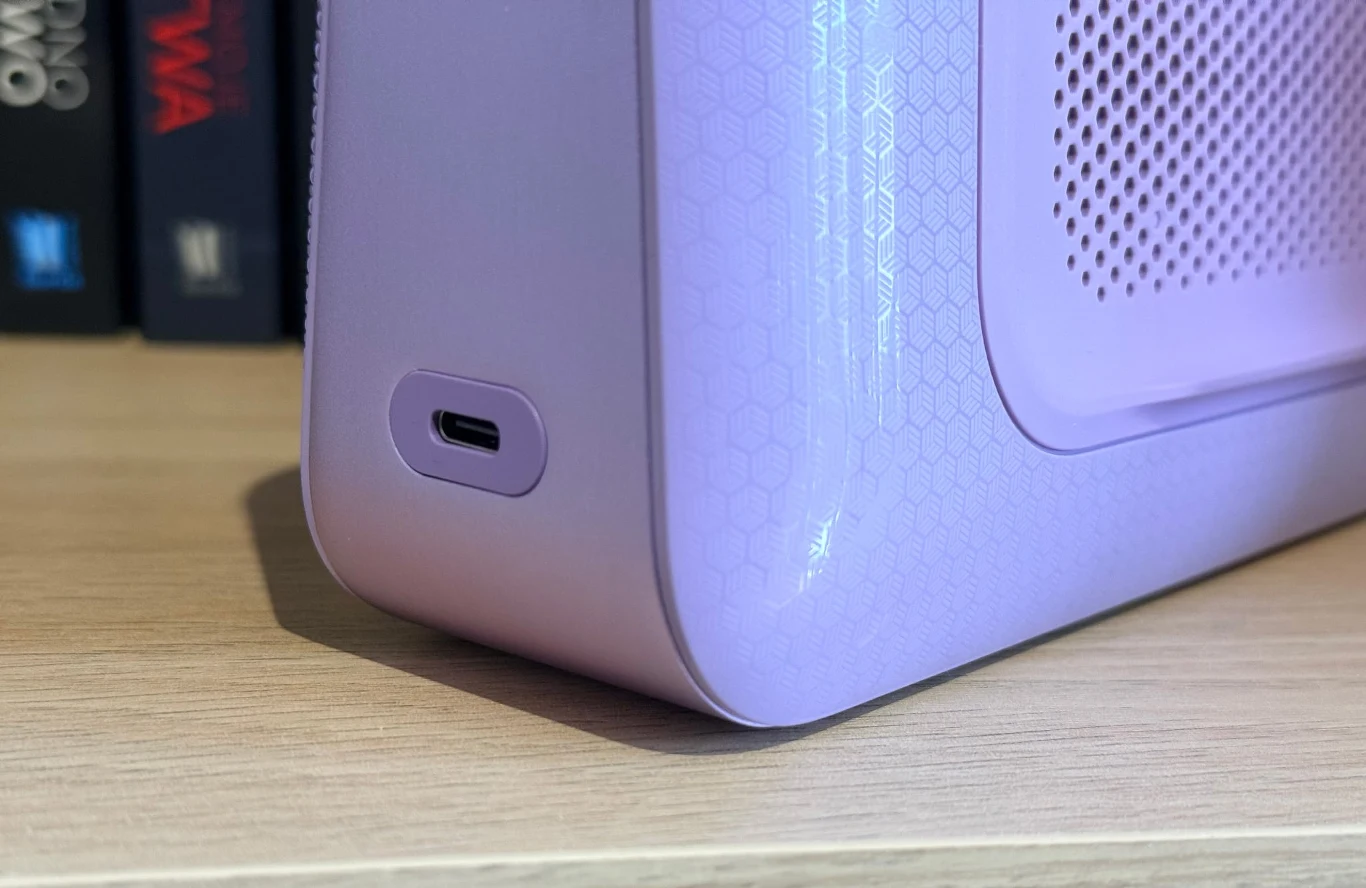 fioletowa obudowa urządzenia elektronicznego z widocznym portem USB-C, ustawiona na drewnianej powierzchni, z fragmentem otworów wentylacyjnych po prawej stronie