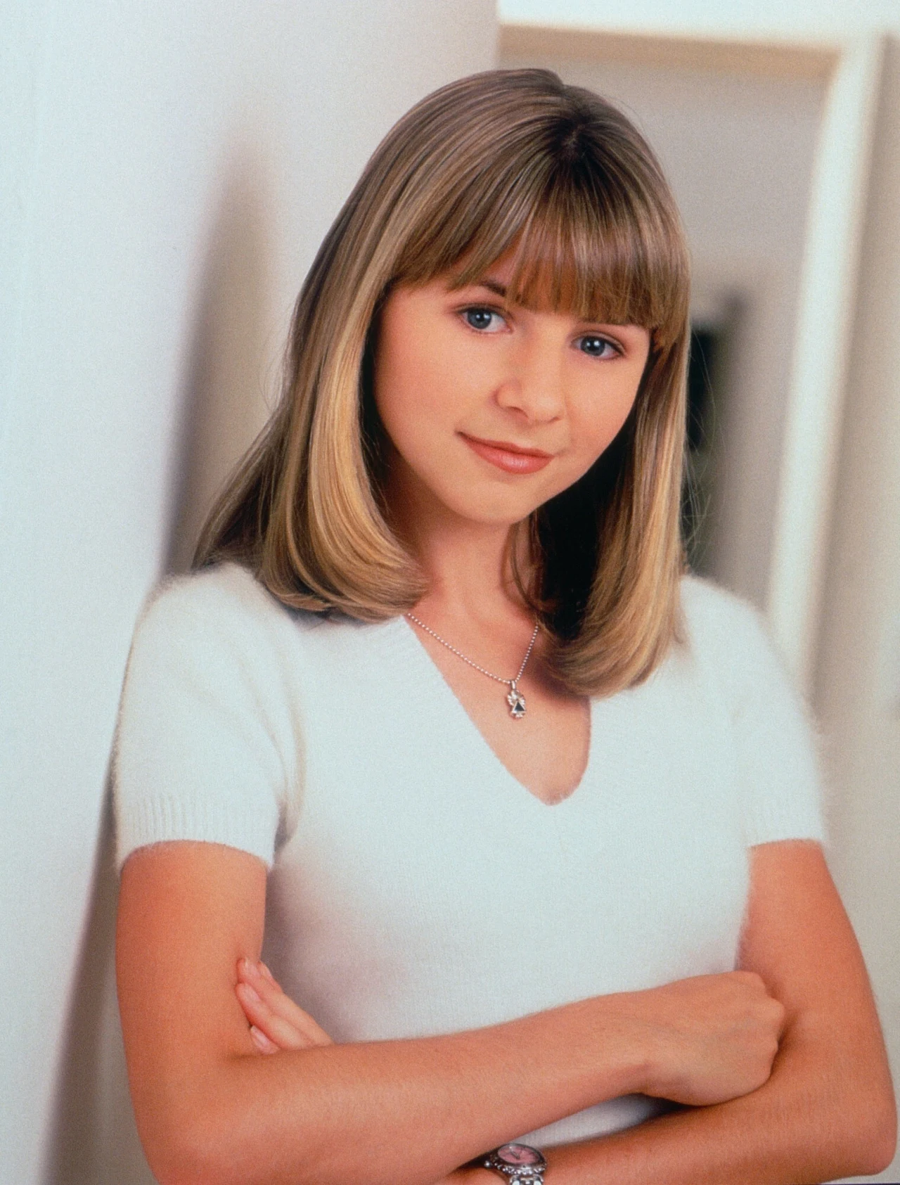 Beverley Mitchell wcielała się w rolę Lucy, córki pastora Młoda kobieta o blond włosach z grzywką, ubrana w białą bluzkę z krótkim rękawem, stoi oparta o ścianę z lekko skrzyżowanymi ramionami, patrzy z lekkim uśmiechem w stronę obiektywu, na szyi ma srebrny naszyjnik.