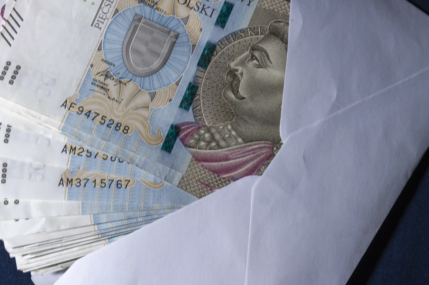 Czy za prezenty komunijne trzeba odprowadzać podatek? Plik banknotów 500 zł wystający z białej koperty.
