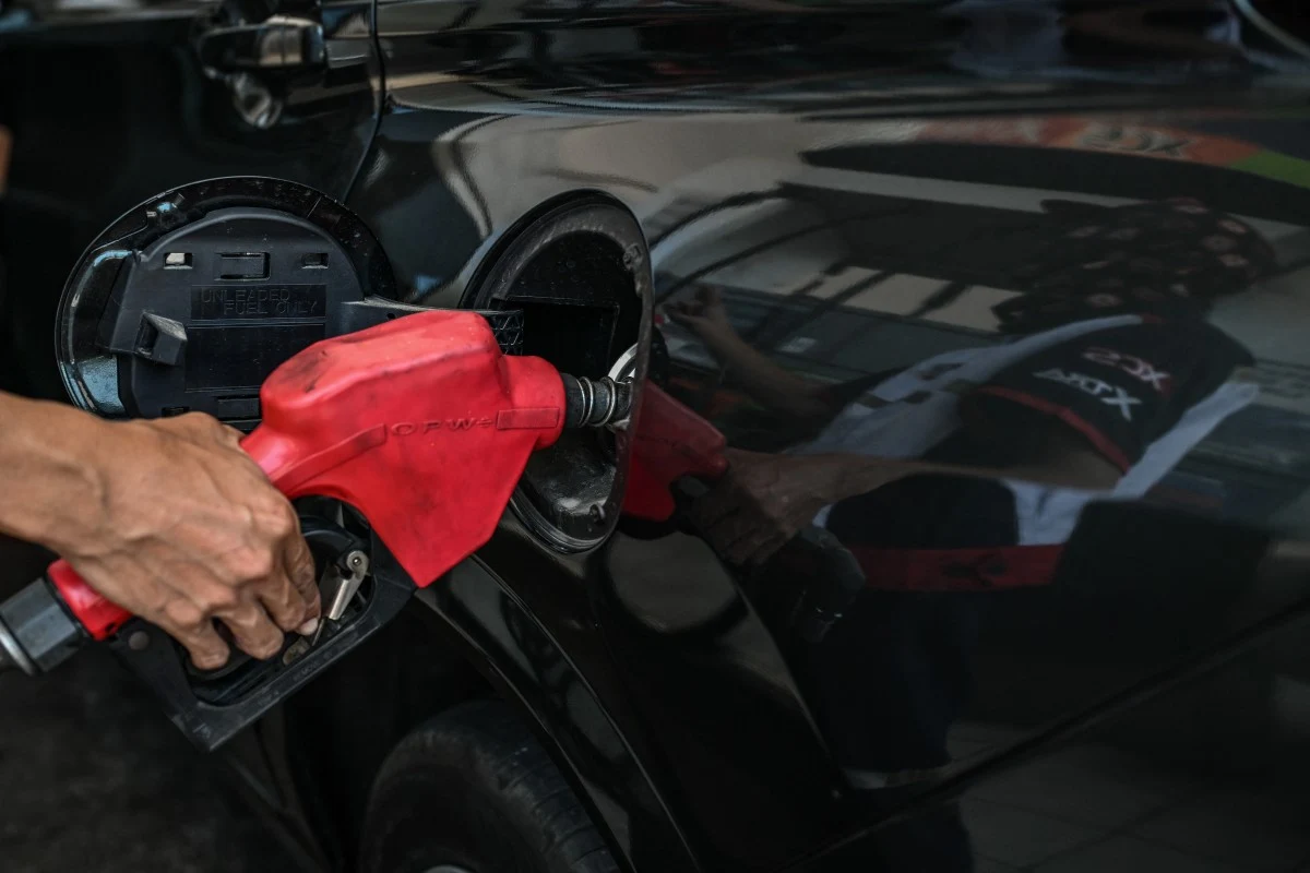 Mimo zawieszenia broni w Iranie Filipińczycy tankują coraz drożej czerwona dysza dystrybutora paliwa wkładana do wlewu czarnego samochodu, odbicie osoby ubraną w białą koszulkę widoczne na lakierze auta