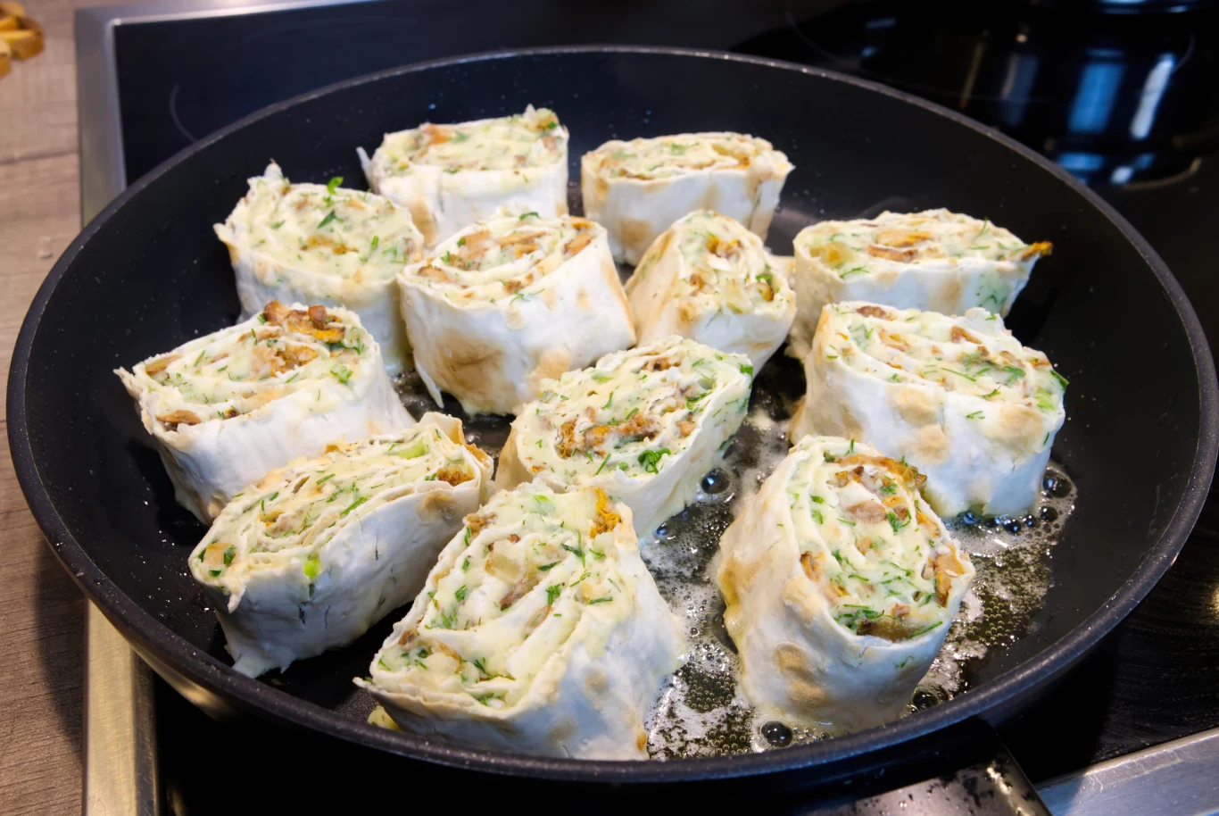 Roladki na ciepło z zewnątrz są chrupiące, a w środku miękkie i soczyste Roladki z kurczakiem, pieczarkami i serem smażone na patelni, panierowane, widoczne zioła w farszu.