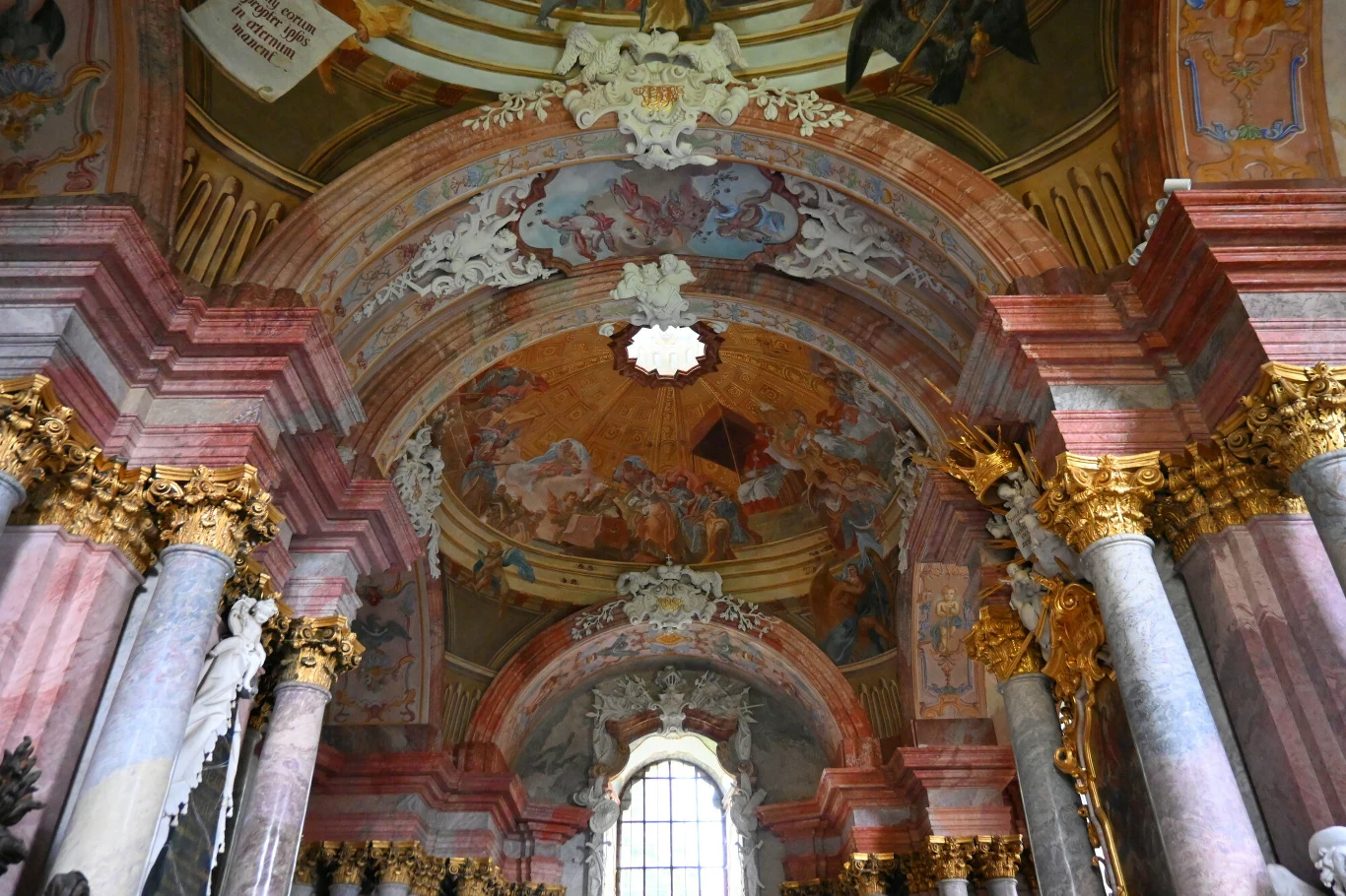 bogato zdobione sklepienie barokowego kościoła z freskami pełnymi scen biblijnych, kolumnami z szarego marmuru ze złotymi kapitelami oraz detalami architektonicznymi w tonacji różowo-czerwonej