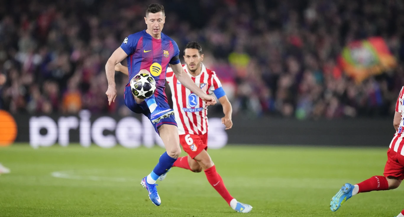 piłkarz w granatowo-bordowej koszulce kontroluje piłkę unosząc ją w powietrzu, otoczony przez zawodników w biało-czerwonych strojach, na tle pełnych trybun stadionu