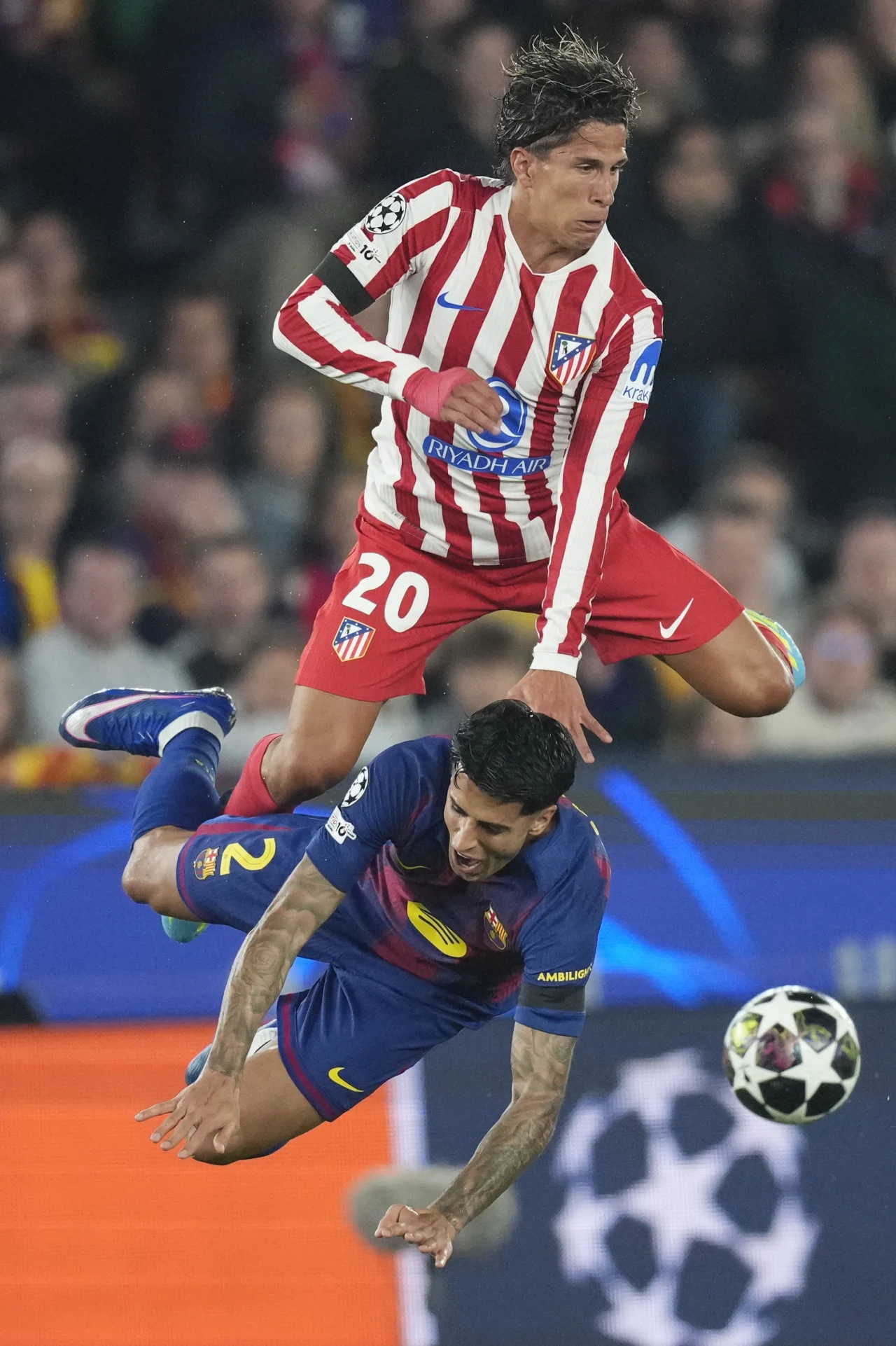 piłkarz w czerwono-białych pasach wykonujący wyskok nad zawodnikiem w granatowo-bordowym stroju, który upada na murawę podczas walki o piłkę podczas meczu