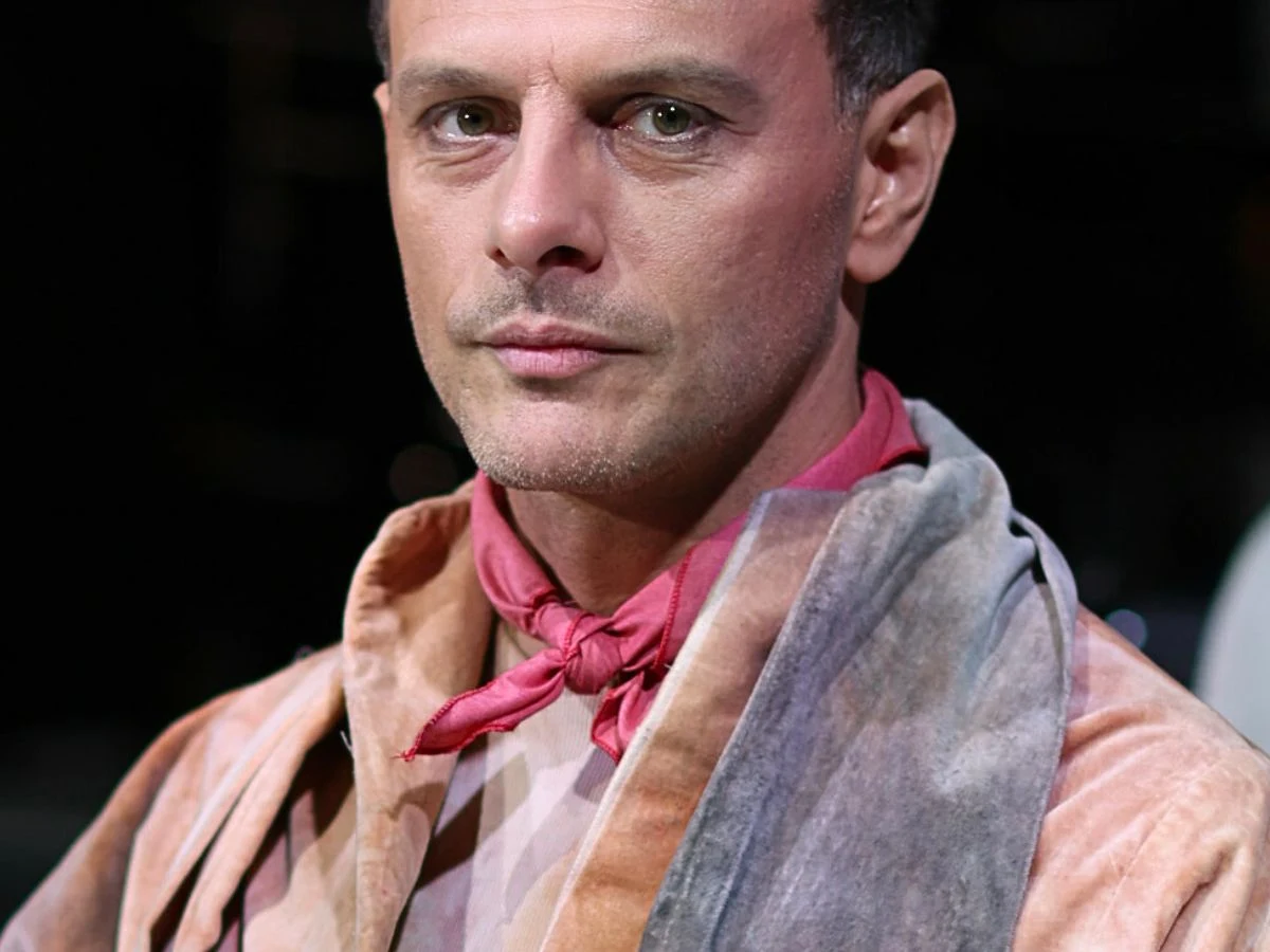 Tomasz Nosiński Tomasz Nosiński w aksamitnym płaszczu pastelowym i różowej apaszce, patrzy w obiektyw aparatu.